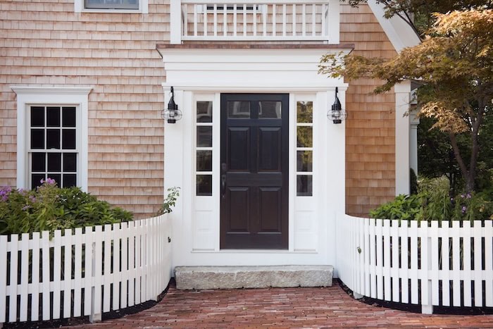 New England South Shore home with light brown shingled exterior and white entranceway and black door
